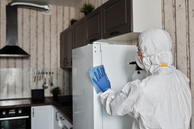 cleaner in white coveralls disinfecting a fridge